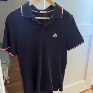 Svart Moncler pikétröja - Svart pikétröja från Moncler med klassisk krage och korta ärmar. Använd ett fåtal gånger och i mycket bra skick