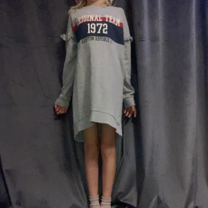 Grå oversized tröja Hampton Republic - Grå oversized sweatshirtklänning från Hampton Republic med tryck 'Original Team 1972' och blå/röda detaljer över bröstet. Långärmad med volangdetaljer på axlarna och rund halsringning. Perfekt för en chill och sportig look. Ps priset är så pga märket.