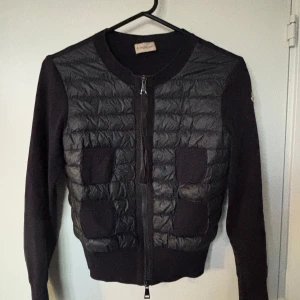 Marinblå moncler cardigan  - Säljer en Moncler cardigan med quiltad framsida och två fickor. Tröjan har långärmade stickade ärmar och dragkedja framtill. Perfekt för lager-på-lager och snygg till både jeans och kjol.