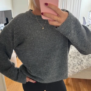 Mörkgrå stickad tröja med rund hals - Mysig mörkgrå stickad tröja med rund hals och långa ärmar. Tröjan har en loose passform och ribbade muddar vid ärmslut och hals. 