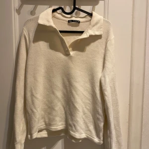 Krämvit tröja från Zara - Snygg tröja från Zara med klassisk krage och två knappar vid halsen. Tröjan har lång ärm och är tillverkad i mjukt, strukturerat material som ger en chill och clean look. Perfekt för dig som gillar enkel och stilren design.