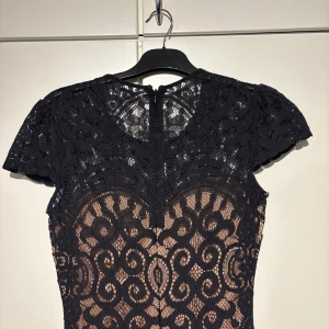Svart lång spetsklänning med mönster - Supersnygg långklänning i svart spets med korta ärmar och figurnära passform. Klänningen har ett detaljerat blommigt mönster och nude-färgad underklänning som ger en cool kontrast. Perfekt för dig som vill sticka ut med elegans och stil. PRIS KAN ALLTID DISKUTERAS!!