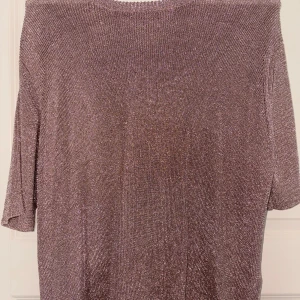 Glittrig topp från Carin Wester - Säljer en glittrig topp från Carin Wester i storlek L. Toppen har en rak passform, halvlånga ärmar och är stickad i ett skimrande material som verkligen fångar ljuset. Perfekt när du vill sticka ut lite extra!
