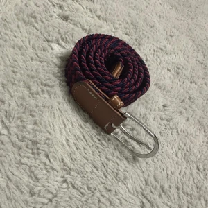 Den är jätte bra de funkar och de är inte sönder eller något - Snyggt flätat bälte i marinblått och vinrött med bruna skinn-detaljer och silverspänne. Bältet har ett randigt mönster och passar perfekt till jeans eller chinos för en stilren look. Flexibelt material som gör det bekvämt att bära hela dagen.
