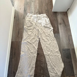 Beiga linnebyxor med snörning - Luftiga beiga linnebyxor med resår och snörning i midjan. Byxorna har raka ben och en avslappnad passform, perfekta för varma dagar. Snygga att matcha med en enkel t-shirt eller skjorta.