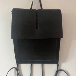 Svart ryggsäck från Carin Wester - Säljer min stilrena svart ryggsäck från Carin wester i skinnimitation med minimalistisk design. Väskan har ett stort lock, silverfärgade metalldetaljer, dragkedja baktill och justerbara axelremmar. Perfekt för dig som gillar en clean och modern look. Nypris 499 därav priset, nästan helt oanvänd bara en liten reva i inne fodret men inget som märks av💕