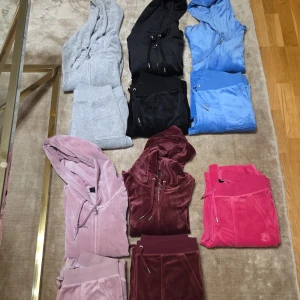 Juicy Couture velour hoodie i flera färger - Juicy Couture velour hoodies med dragkedja och snörning i flera färger: grå, svart, blå, ljusrosa, vinröd och ceriserosa. Klassisk hoodie med huva, ribbade muddar och logga broderad på bröstet. Perfekt för en chill och trendig look.