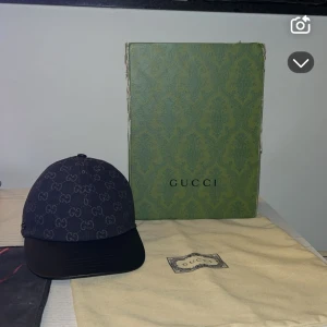 Gucci keps - Säljer en svart keps från Gucci i storlek S, med klassiskt GG-monogram över hela kepsen. Kepsen har böjd skärm och justerbar rem bak. Tillverkad i Italien och levereras med originalkartong och dustbag. Perfekt för dig som vill ha en lyxig och stilren accessoar.
