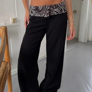 Svarta wide byxor med zebramönster - Snygga svarta byxor med bred passform och låg midja. Linningen har ett coolt zebramönster i svart och grått som ger en unik touch. Perfekta för dig som vill sticka ut med en trendig och bekväm look.