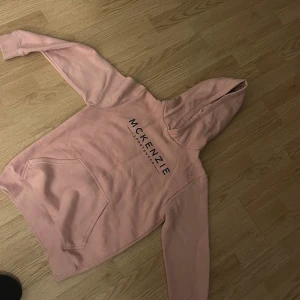 Rosa hoodie från McKenzie - Säljer en snygg ljusrosa hoodie från McKenzie med svart tryck på bröstet. Tröjan har huva, magficka och långa ärmar. Perfekt för chill dagar eller när du vill ha en avslappnad stil. Storlek 13-15 år sitter som storlek S