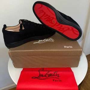 Christian Louboutin svarta sneakers med nitar - Svarta sneakers från Christian Louboutin i mocka med ikoniska röda sulor och svarta nitar på tån. Skorna har snörning och rund tå, samt exklusiv känsla med märkets logga på innersulan. Perfekta för dig som vill sticka ut med en lyxig och edgy stil. (SKORNA ÄR ALDRIG ANVÄNDA) fraktar alltid inom några timmar. Finns ett verkligt kvitto och ett på mailen!