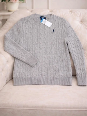 Grå kabelstickad tröja Polo Ralph Lauren - Säljer en snygg grå kabelstickad tröja från Polo Ralph Lauren i storlek S. Tröjan har rund hals, långärmad design och klassisk broderad logga på bröstet. Perfekt för dig som gillar stilrena och tidlösa plagg med premiumkänsla.