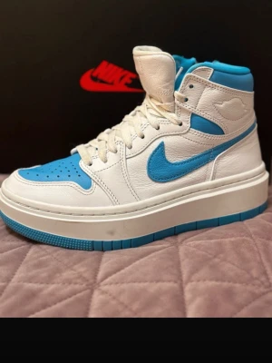 Nike Air Jordan 1 High vit/blå - Säljer ett par Nike Air Jordan 1 High sneakers i vitt och blått skinn. Klassisk siluett med högt skaft, perforerad tåbox och blå swoosh på sidan. Skorna har vit snörning och en rejäl vit/blå yttersula som ger grym streetstil.