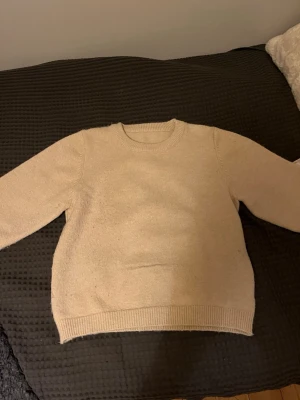 Beige stickad tröja i ullmix - Enkel och stilren beige stickad tröja med rund hals och ribbade muddar vid ärmslut och nederkant. Perfekt för lager på lager under höst och vinter. Mjuk och skön känsla, passar till allt.