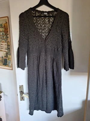 Grå stickad kofta - Mysig grå stickad kofts med v-ringning och knappar framtill. Klänningen har trekvartsärm och ett fint hålmönster upptill. Perfekt för lager på lager och passar till många olika stilar. Djur finns i hemmet