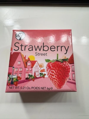 Strawberry Street rouge från W7 - Rouge i en söt fyrkantig ask med jordgubbsdesign. Färgen är en varm, bärig rosa med lätt skimmer som ger kinderna en fräsch glow. Innehåller 6g puderrouge som är enkel att blenda ut för ett naturligt resultat.