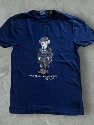 Polo Bear t-shirt Ralph Lauren - Snygg mörkblå t-shirt från Polo Ralph Lauren med ikoniskt Polo Bear-motiv på bröstet. Modellen är custom slim fit och har korta ärmar. Tillverkad i mjuk bomull och perfekt för en stilren look. Köpt i Ralph Laurens butik.