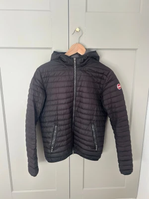 Svart pufferjacka från Colmar - Säljer en svart pufferjacka från Colmar med huva och två dragkedjeförsedda fickor. Jackan har ett quiltat mönster och Colmar-logga på ärmen. Perfekt för kyliga dagar och riktigt snygg till jeans eller sweatpants. Storlek för 14y ( 166cm ) men passar även en Xss/xs 