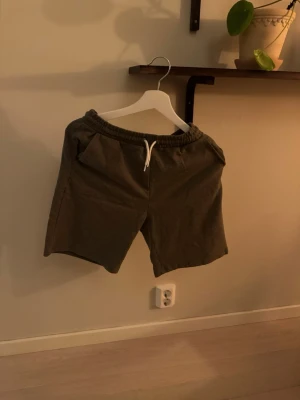 Gråa shorts från Lindex med snörning - Mysiga gråa shorts från Lindex med elastisk midja och vit snörning. Perfekta för chill dagar eller när du vill ha det bekvämt. Tillverkade i mjuk bomull och har en loose fit som ger skön rörelsefrihet.