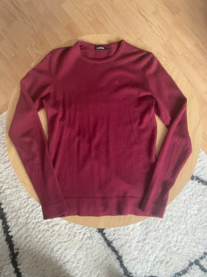 Röd Cashmere från J.Lindeberg - Tjabba👋 Säljer en vinröd cashmere tröja från J.Lindeberg i storlek S men som tyvärr har krympt till XS!📐Tröjan har rund halsringning, lång ärm och diskret broderad logga på bröstet🪢 Perfekt till höst och vinter för en clean och stilren look😤 OBS! Det finns ett pytte litet hål på bakre axel! Vid frågor: Meddela oss!💌