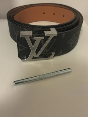 Svart bälte med mönster och ett silvrigt spänne - Säljer ett helt nytt svart bälte med blommor på och ett silvrigt spänne storlek 115cm man får även med en liten spik som man kan göra extra hål med 