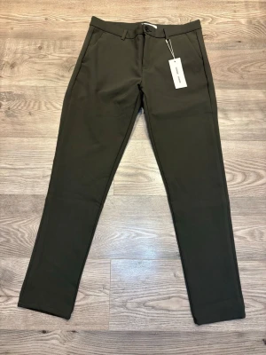 Samsøe Samsøe - Snygga gröna kostymbyxor från Samsøe Samsøe i modellen Frankie Pants. Byxorna har en rak passform, midwaist, klassiska fickor och stängs med knapp och dragkedja. Materialet är mjukt och har en lätt stretch, perfekt för en clean och stilren look.