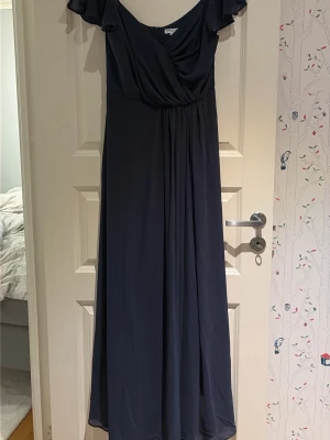 Marinblå långklänning från Bubbleroom - Säljer en marinblå långklänning från Bubbleroom med omlottliv och v-ringning. Klänningen har volangärmar och ett fint fall i kjolen. Perfekt för speciella tillfällen och har en dragkedja i ryggen. Materialet känns lätt och luftigt. Pris kan diskuteras