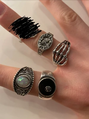 Fyra coola silvriga ringar - Säljer ett set med fyra unika silvriga ringar. En ring har ett skelettmotiv, en har en svart åtta-boll, en har ett ovalt skimrande steninlägg med detaljer runt och en har ett mönstrat motiv. 8kr styck eller alla för 30kr! 🫶 ej äkta silver