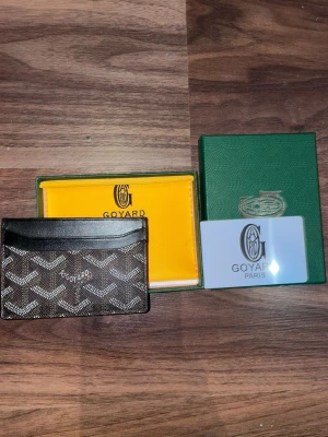 G-yard plånbok med klassiskt mönster - Säljer en snygg och stilren plånbok från G-yard med det ikoniska rutiga mönstret i svart, brunt och vitt. Plånboken är tillverkad i skinn och har flera fack för kort. Kommer med original ask och certifikat. Perfekt för dig som gillar exklusiva accessoarer.