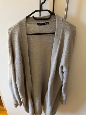 Beige/grå kofta från lager 157 - Mysig och enkel beige kofta från lager 157 i storlek xs/s. Koftan har lång ärm, öppen framtill och är tillverkad i ett mjukt stickat material. Perfekt att slänga på sig när det är lite kyligt ute. Snygg att matcha med jeans eller leggings. Lite knopprig går att fixa