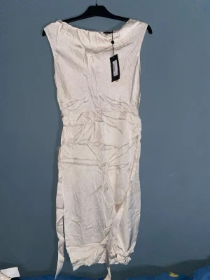 Vit sidenklänning från STOCKH LM - Supersnygg vit långklänning från STOCKH LM i glansigt sidenmaterial. Klänningen har en enkel, elegant design med bred halsringning och markerad midja. Perfekt för dig som vill ha en stilren look med lyxig känsla.