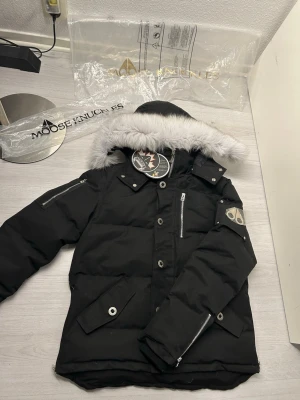 Svart Moose Knuckles dunjacka med pälskrage - Säljer en svart dunjacka från Moose Knuckles med stor grå pälskant på huvan och flera snygga detaljer som dragkedjor, knappar och patch på ärmen. Jackan har broderad insida och praktiska fickor. Perfekt för kalla dagar och riktigt stilren. Den har två fickor på insidan av jackan men ser inte så mycket den andra fickan. Väldigt varm som jacka perfekt för kalla dagar. Man kan också ta av den vita pälsen och luvan. Överiga frågor eller om ni vill få mer bilder kontakta gärna mig ;)