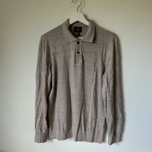 Beige pikétröja i bomull från H&M - Klassisk beige pikétröja från H&M i 100% bomull. Tröjan har lång ärm, krage och knäppning med tre knappar framtill. Perfekt för en clean och stilren look, passar till både jeans och chinos. 2K8