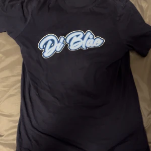 Mörkblå Di Blå t-shirt med tryck - Snygg mörkblå t-shirt från Di Blå med stort, stilrent tryck i ljusblått och vitt på bröstet. Klassisk rund hals och korta ärmar. Materialet känns mjukt och skönt, perfekt för dig som gillar enkel och cool streetstil.