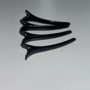 Svarta hårklämmor i plast - Fyra svarta hårklämmor med stilren och smal design, perfekta för att hålla håret på plats. Klämmorna är tillverkade i blank plast och har en enkel metallfjäder för smidig användning. Passar både till att styla och dela upp håret vid fix. Har ej använt dem mycket. Pris diskuteras 