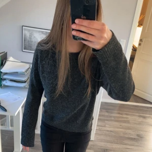 Mörkgrå stickad tröja - Mysig mörkgrå stickad tröja med rund halsringning och långa ärmar. Tröjan har en klassisk passform och ribbade muddar vid ärmslut och nederkant.