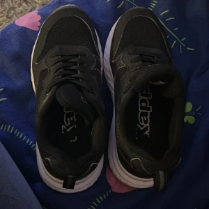 Svarta sneakers från Kappa - Säljer ett par svarta sneakers från Kappa med vit sula. Skorna har snörning och är tillverkade i syntetmaterial och mesh för en sportig look. Perfekta för dig som gillar stilrena och bekväma skor till vardags. Klassisk rund tå och platt sula.