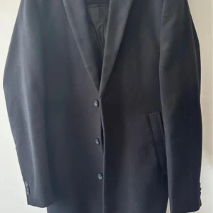 Svart rock från New Look Men, stl S - Klassisk svart rock från New Look Men i storlek S. Jackan har tre knappar framtill, breda slag och två snedställda fickor. Perfekt för dig som vill ha en stilren och tidlös look. Materialet är mjukt och känns lyxigt.