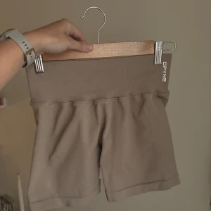Beige seamless shorts från DFYNE - Säljer ett par beige seamless shorts från DFYNE med hög midja och ribbad linning. De är tillverkade i ett stretchigt material av polyamid och elastan, perfekta för träning eller chill. Snygg minimalistisk look med liten logga på linningen. Är även från en limited edition kollektion med Hanna Pearsson 