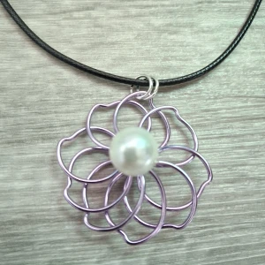 Handgjort halsband med lila blomma  - Handgjort unikt halsband med svart snöre och ett blommigt hänge gjort av lila metalltråd. I mitten sitter en vit pärla som ger en elegant touch. Blomman är ca 3.5cm stort,kedjan på halsbandet är justerbart.Perfekt för dig som vill sticka ut med ett kreativt och färgglatt smycke.
