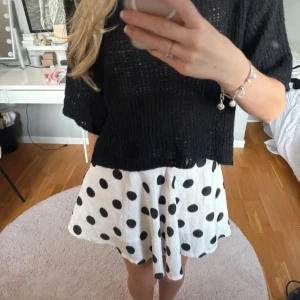 Vit kortkjol med svarta prickar - Supersöt vit kortkjol med stora svarta prickar och skön, flowy passform. Kjolen är tillverkad i ett lätt material som ger en snygg siluett. Väldigt trendig. Lite volangig i passformen.