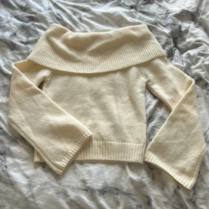 Offshoulder stickad tröja i creme - Superfin offshoulder stickad tröja i cremevitt med bred ribbad kant upptill. Tröjan har lång ärm och sitter figurnära över kroppen. (Helt oanvänd) 