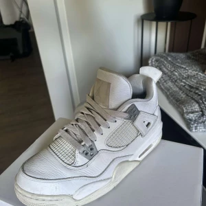 Nike Air Jordan 4 Retro Vit EUR 40 - Säljer ett par Nike Air Jordan 4 Retro i helvitt skinn med meshpaneler och grå detaljer. Klassisk siluett med snörning, platt sula och ikonisk Jumpman-logga under sulan. Perfekta för dig som gillar streetwear och sneakers med retrovibbar.