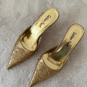 Guldiga klackar från Golden Peak - Säljer ett par guldiga klackar från Golden Peak med spetsig tå och låg klack. Skorna har broderade detaljer och små pärlor. Passar en storlek 36/37