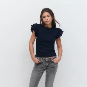 Svart topp med volangärmar - Supersnygg svart topp med volangdetaljer på axlarna och rund halsringning. Ärmlös modell med broderade volanger som ger en cool och trendig look. Perfekt att styla med jeans eller kjol för en uppdaterad outfit.