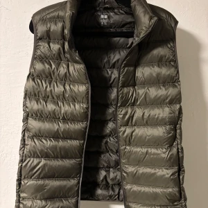 Olivgrön dunväst från Uniqlo S - Snygg olivgrön dunväst från Uniqlo Ultra Light Down. Västen är quiltad med horisontella sömmar, har hög krage och är superlätt. Perfekt att slänga över en hoodie eller tröja när det är kyligt ute.