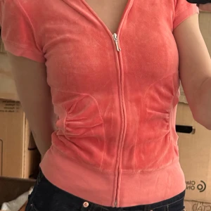 Vintage Juicy Couture rosa velour hoodie - Juicy Couture hoodie i mjuk rosa velour med korta puffärmar, dragkedja framtill och huva. Snygga rynkade fickor på sidorna och bred mudd nedtill.