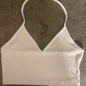 Vit ribbad linnetopp med smala axelband - Snygg vit ribbad linnetopp med smala axelband och v-ringning. Toppen är croppad och har en enkel, stilren design som passar perfekt till jeans eller kjol. Materialet är stretchigt och bekvämt.