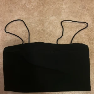 Svart croppad topp från SHEIN - Säljer en svart croppad topp från SHEIN med tunna axelband. Enkel och stilren design som är lätt att matcha med olika outfits. Toppen har en rak form och är tillverkad i ett mjukt syntetmaterial.