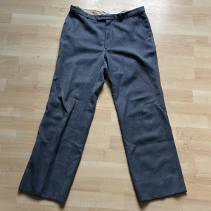 Grå kostymbyxor med diskret mönster - Snygga grå kostymbyxor från Urban med diskret randigt mönster. Byxorna har rak passform, bälteshällor och stängs med dragkedja och knapp. Perfekta för en clean och stilren look. Materialet känns mjukt och har en klassisk känsla.